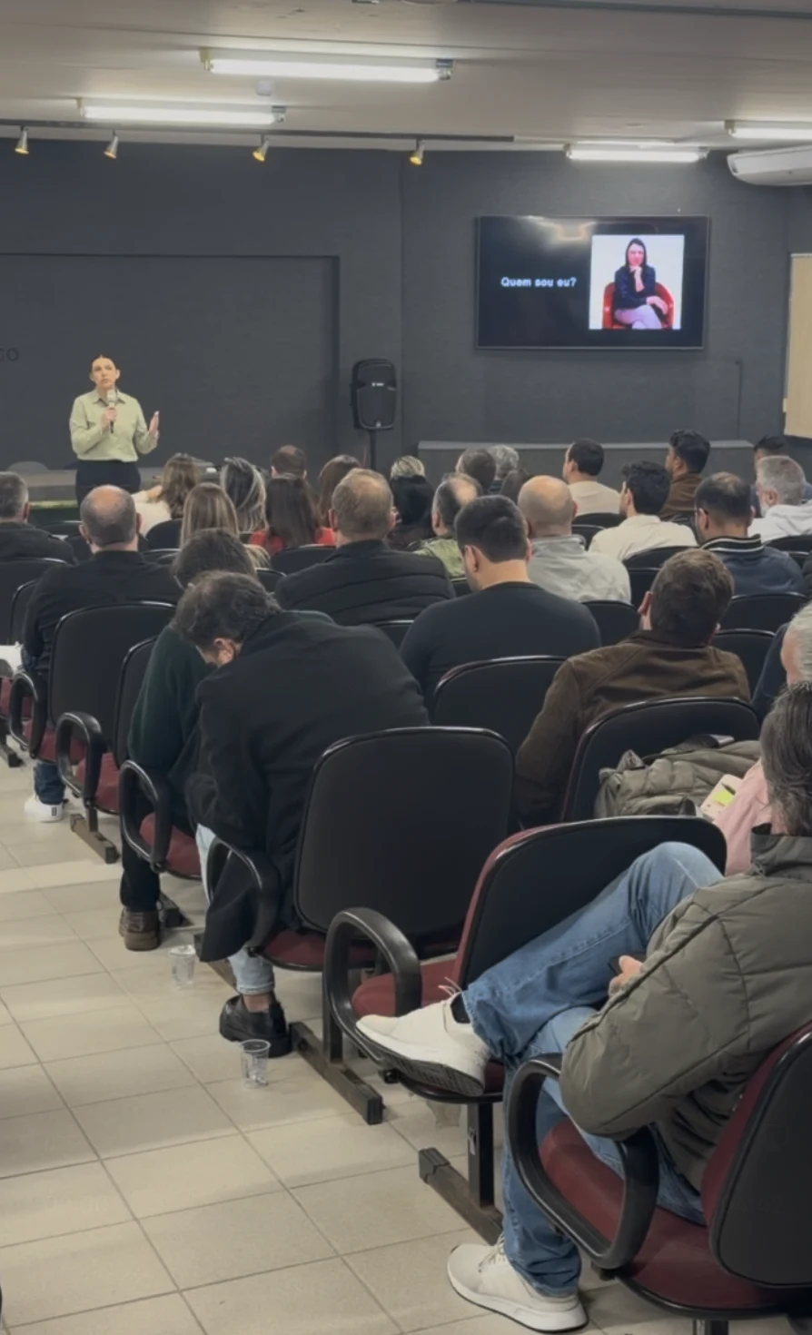 Cleide conduzindo uma palestra presencial para corretores, com o auditório ocupado